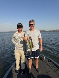 Two anglers proudly displaying a large Largemouth Bass while fishing on a lake.