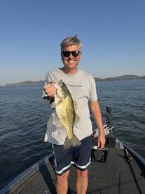 A happy angler proudly displaying a large Largemouth Bass while fishing on a sunny day.