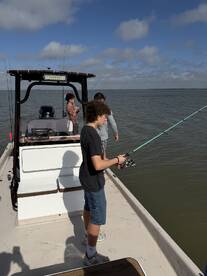 A group of anglers enjoying a fishing trip on a boat, with a young boy actively reeling in a catch in a scenic fishing environment.