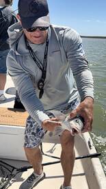 Angler holding a freshly caught fish while fishing on a boat in a coastal environment.