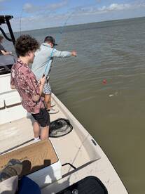 A young angler and an adult are actively fishing from a boat, with one person reeling in a catch while the other prepares to assist. The scene captures the excitement of fishing in a coastal environment.