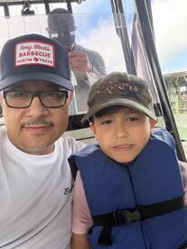 A father and son enjoying their time on a fishing boat, with the son wearing a life jacket and a cap, ready for an exciting fishing adventure.