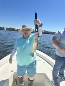 An angler proudly displaying a Speckled Trout while fishing from a boat on a sunny day.