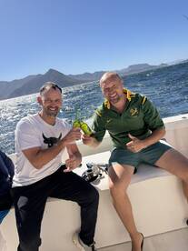 Two anglers enjoying drinks on a boat, with scenic mountains in the background, capturing a relaxed fishing atmosphere.