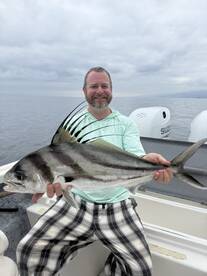 Angler proudly displaying a large Roosterfish while fishing on a boat, showcasing a successful day on the water.