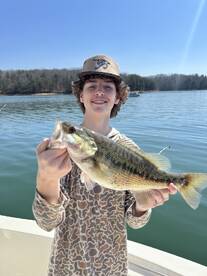 A young angler proudly displaying a large Largemouth Bass while fishing on a serene lake.