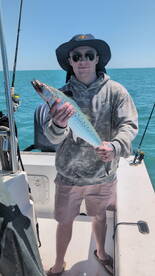 Angler proudly displaying a large Spanish Mackerel while fishing on a sunny day.