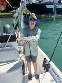 Young angler proudly holding a spotted sea trout while fishing from a boat in a coastal waterway.
