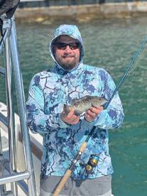 Angler proudly displaying a caught fish while fishing from a boat in clear waters.