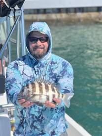 Angler proudly displaying a striped Sheepshead caught while fishing from a boat.