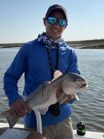 Angler proudly displaying a large Redfish while fishing in a scenic coastal environment.