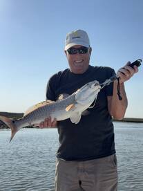 An angler proudly displaying a large Redfish while fishing in a coastal environment.