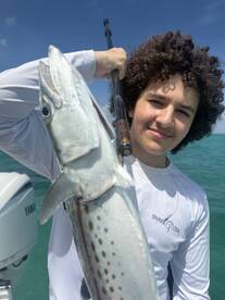Young angler proudly holding a large fish while fishing on a boat in clear waters.