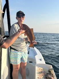 A smiling angler proudly displaying a caught fish while fishing on a boat in open waters.