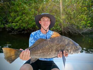A young angler proudly displaying a large Black Drum caught while fishing in a lush mangrove environment.
