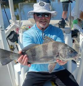 Angler proudly displaying a large Black Drum while fishing on a boat, showcasing a successful day on the water.