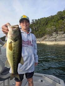 A young angler proudly displaying a large Largemouth Bass while fishing on a scenic lake.