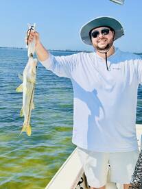 Angler proudly displaying a Snook caught while fishing from a boat in clear waters.