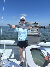 A young angler proudly displaying a large King Mackerel while fishing on a sunny day.