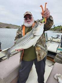 An angler proudly displaying a large striped bass while fishing from a boat, showcasing a successful catch in a serene waterway.
