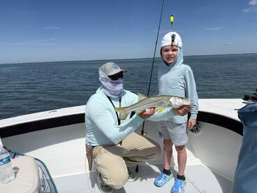 A young angler proudly displays a Snook while fishing on a boat in a coastal waterway.