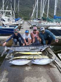 A family proudly displaying their catch, including a large Marlin and several Mahi-Mahi, at the marina after a successful fishing trip.