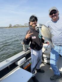Two anglers proudly displaying a large Striped Bass while fishing on a lake, showcasing a fun and successful outing.
