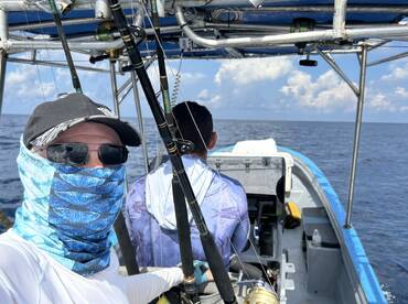 Two anglers aboard a fishing boat, with one at the helm and the other preparing for a fishing adventure in open waters.
