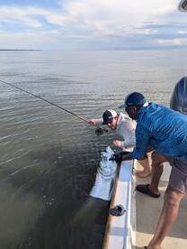 Two anglers working together to reel in a large fish while fishing in calm waters, showcasing an exciting moment on the boat.