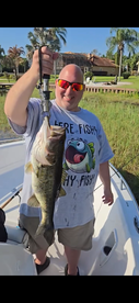 Angler proudly displaying a large Largemouth Bass while fishing from a boat in a scenic waterway.