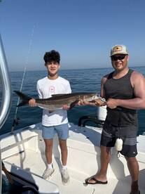 A young angler and an adult proudly displaying a large fish on a boat during a fishing trip.