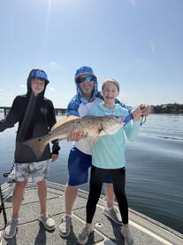 A family proudly displays a large Redfish on a boat, enjoying a sunny day on the water.