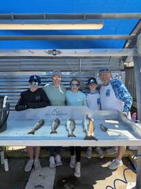A family poses proudly in front of their catch, showcasing several Redfish on a display table at a marina.