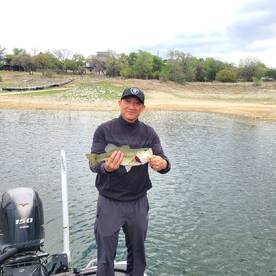 Angler proudly displaying a large Largemouth Bass while fishing from a boat in a serene lake setting.