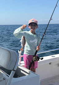 Young angler proudly holding a Snapper while fishing on a boat in open waters.