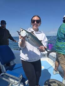 A young angler proudly displaying a caught Bonito while fishing on a boat, enjoying a sunny day at sea.