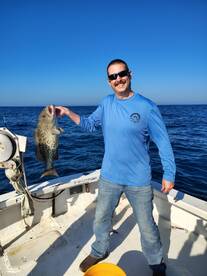 Angler proudly displaying a large Grouper while fishing offshore, showcasing a clear blue sky and calm waters.