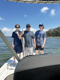 A family proudly displaying a Speckled Trout while fishing on a boat in a scenic waterway.
