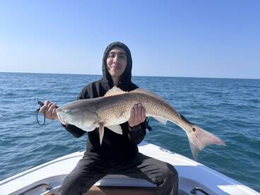 A young angler proudly displaying a large Redfish while fishing on a boat in open waters.