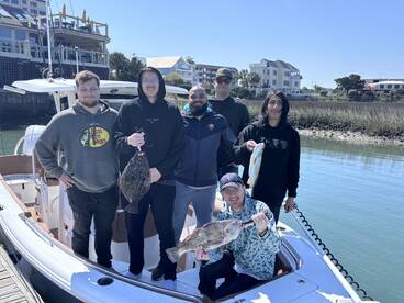 Group of anglers proudly displaying their catch, including a Flounder and a Snapper, aboard a boat in a coastal fishing environment.