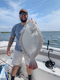 Angler proudly displaying a large Flounder while fishing on a sunny day in a coastal waterway.
