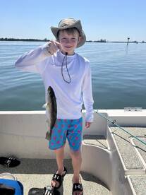 Young angler proudly holding a Speckled Trout while fishing on a sunny day.