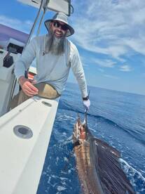 Angler reeling in a large Sailfish while enjoying a sunny day on the open ocean.