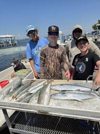 A group of anglers, including two young boys, proudly display their catch of Speckled Trout and Spanish Mackerel on a boat after a successful fishing trip.