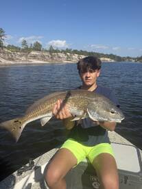 A young angler proudly displaying a large Redfish while fishing in a scenic river environment.