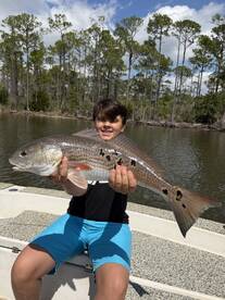 A young angler proudly displaying a large Redfish while fishing in a scenic river environment.