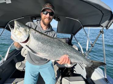 Angler proudly displaying a large Salmon while aboard a fishing boat, showcasing a successful day on the water.