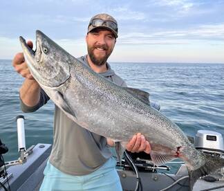 Angler proudly displaying a large Chinook Salmon while fishing on a boat in open waters.