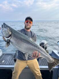 Angler proudly displaying a large Salmon while fishing on a boat, showcasing a successful day on the water.