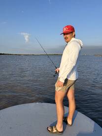 Angler casting a line from the bow of a boat in calm waters, enjoying a day of fishing under a clear blue sky.